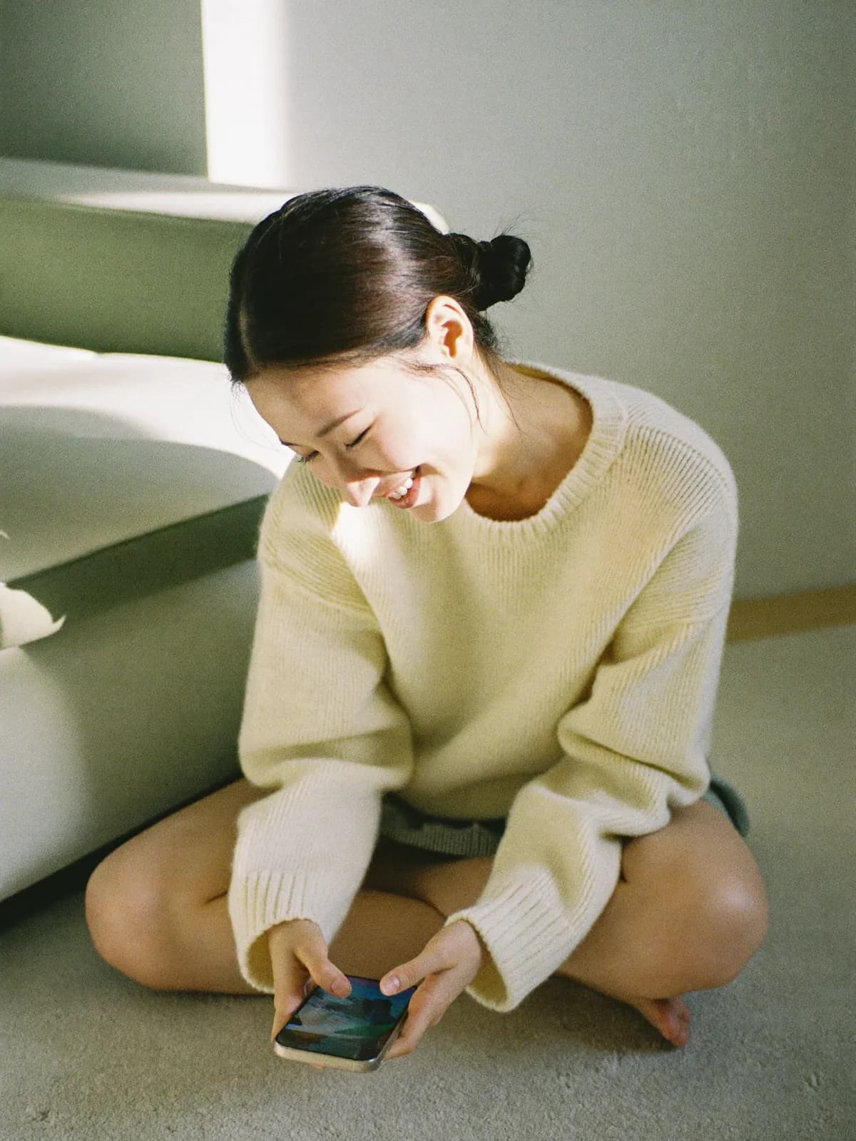 A woman sitting on the floor at home, smiling at her phone