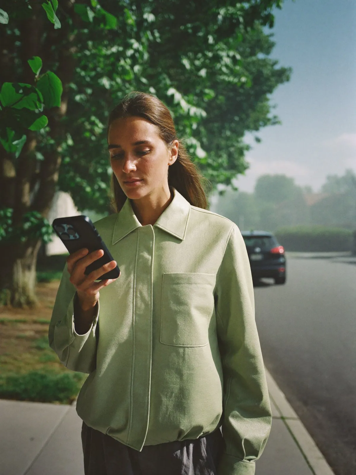 A woman on a morning walk under the trees, reading her phone
